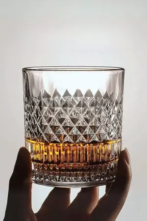 verre à whisky cristal tumbler tenu en main avec fond clair