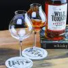 Verre à whisky tulipe posé sur sous-verre en pierre, avec bouteille de bourbon Wild Turkey en arrière-plan.