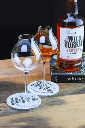 Verre à whisky tulipe posé sur sous-verre en pierre, avec bouteille de bourbon Wild Turkey en arrière-plan.