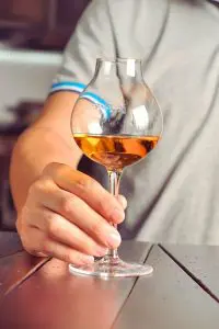 Verre à whisky tulipe tenu à la main au-dessus d’une table en bois foncé.
