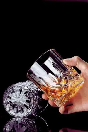 Verre à whisky en cristal sculpté tenu à la main, révélant son design raffiné.