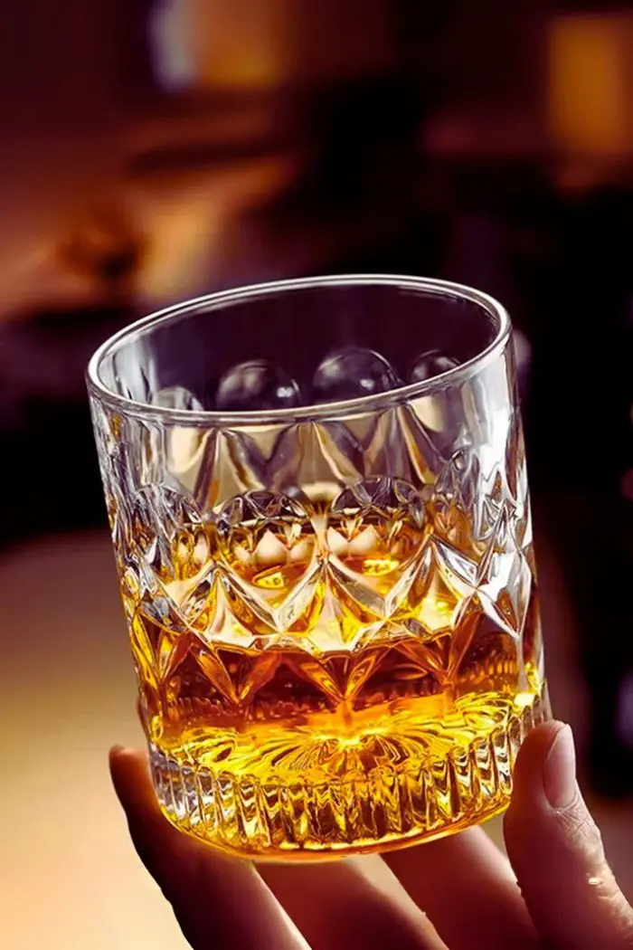 verre à whisky cristal 330 ml tenu en main avec fond flou et ambiance chaleureuse