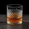 Verre à whisky cristal tumbler posé sur une surface en bois foncé, rempli partiellement de whisky ambré.