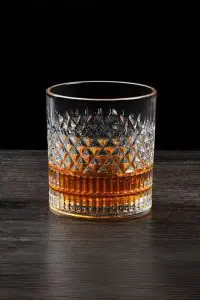 Verre à whisky cristal tumbler posé sur une surface en bois foncé, rempli partiellement de whisky ambré.