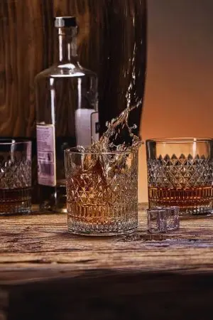 Verre à whisky cristal tumbler sur une table en bois rustique, avec un whisky éclaboussant en plein mouvement.