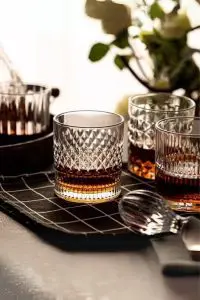 Verre à whisky cristal tumbler posé sur une nappe quadrillée noire, accompagné de trois autres verres assortis.