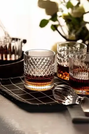 Verre à whisky cristal tumbler posé sur une nappe quadrillée noire, accompagné de trois autres verres assortis.