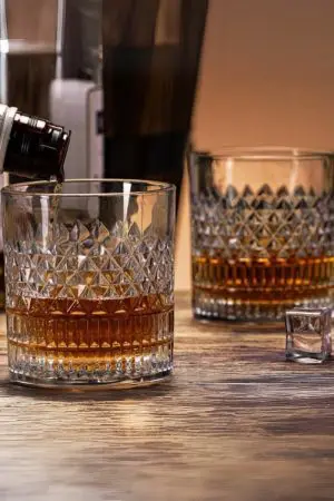 Verre à whisky cristal tumbler en cours de remplissage sur une table en bois, avec un autre verre posé à côté.