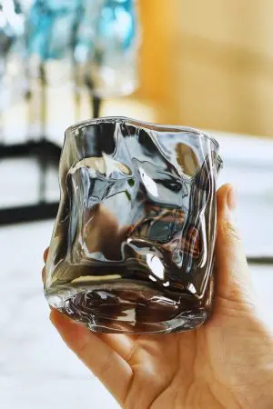 verre à whisky moderne noir fumé tenu à la main devant un fond lumineux
