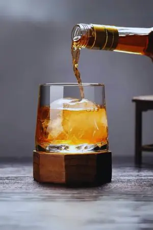 Verre à whisky en cristal rempli de whisky - Base en bois et design raffiné.