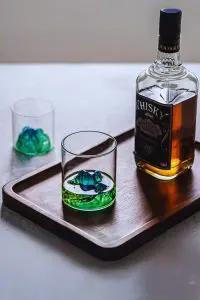 Verre à whisky japonais vert montagneux, posé sur plateau, rempli de whisky