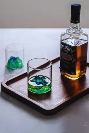 Verre à whisky japonais vert montagneux, posé sur plateau, rempli de whisky