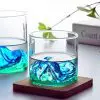 Verre à whisky design montagne vert rempli, posé sur un sous-verre en bois