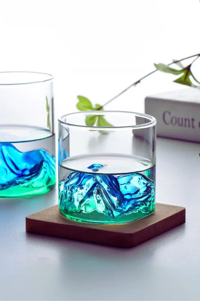 Verre à whisky design montagne vert rempli, posé sur un sous-verre en bois