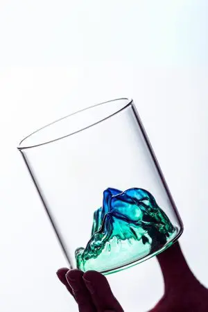 Verre à whisky design montagne vert tenu incliné à la main, vide
