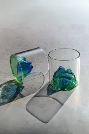 Verres à whisky design montagne vert posés sur une surface claire, l’un debout, l’autre allongé