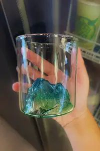 Verre à whisky montagne verte et bleue tenu dans une main devant une lumière intérieure