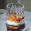 verre à whisky tumbler design texturé posée sur une surface métallique avec whisky ambré