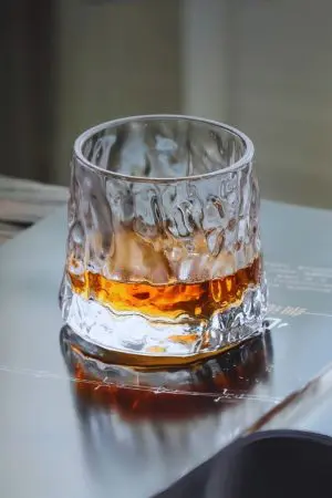 verre à whisky tumbler design texturé posée sur une surface métallique avec whisky ambré