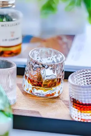 verre à whisky tumbler en forme de glaçon rempli posé sur plateau en bois avec autres verres