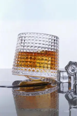 Verre à whisky tumbler incliné sur surface miroir avec liquide ambré