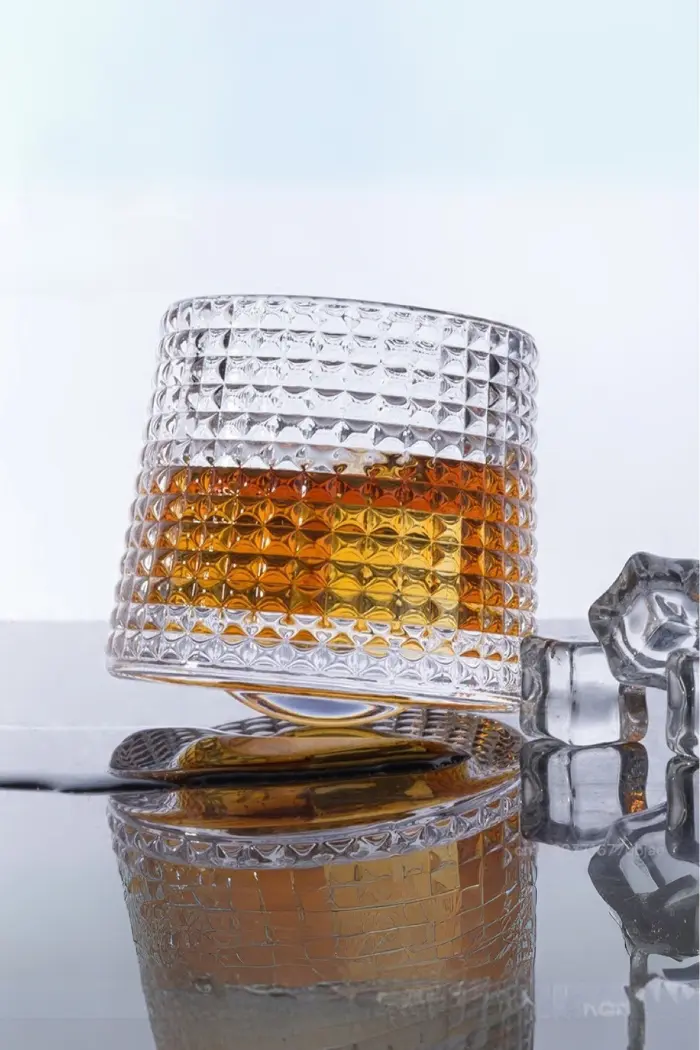 Verre à whisky tumbler incliné sur surface miroir avec liquide ambré