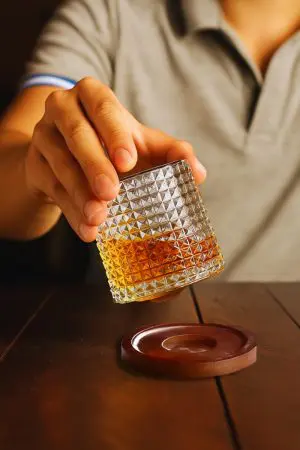 Verre à whisky tumbler tenu à la main au-dessus d’un socle rond en bois