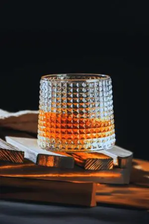 Verre à whisky tumbler posé sur planche de bois avec éclairage tamisé