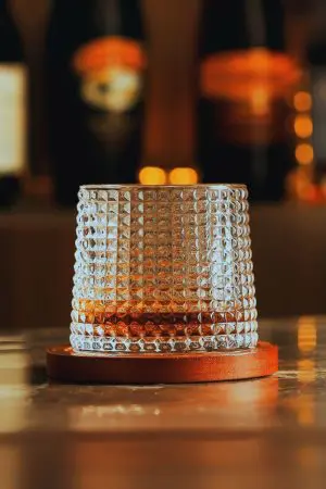 Verre à whisky tumbler posé sur socle rond en bois dans ambiance tamisée
