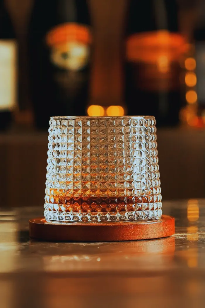 Verre à whisky tumbler posé sur socle rond en bois dans ambiance tamisée