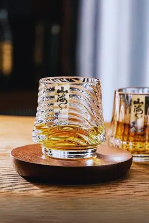 Verre à whisky japonais posé sur support en bois avec base ondulée inspirée de la mer