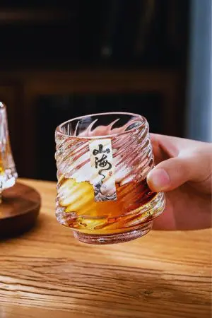 Verre à whisky rempli, dans la main, glaçons visibles et motif marin à la base