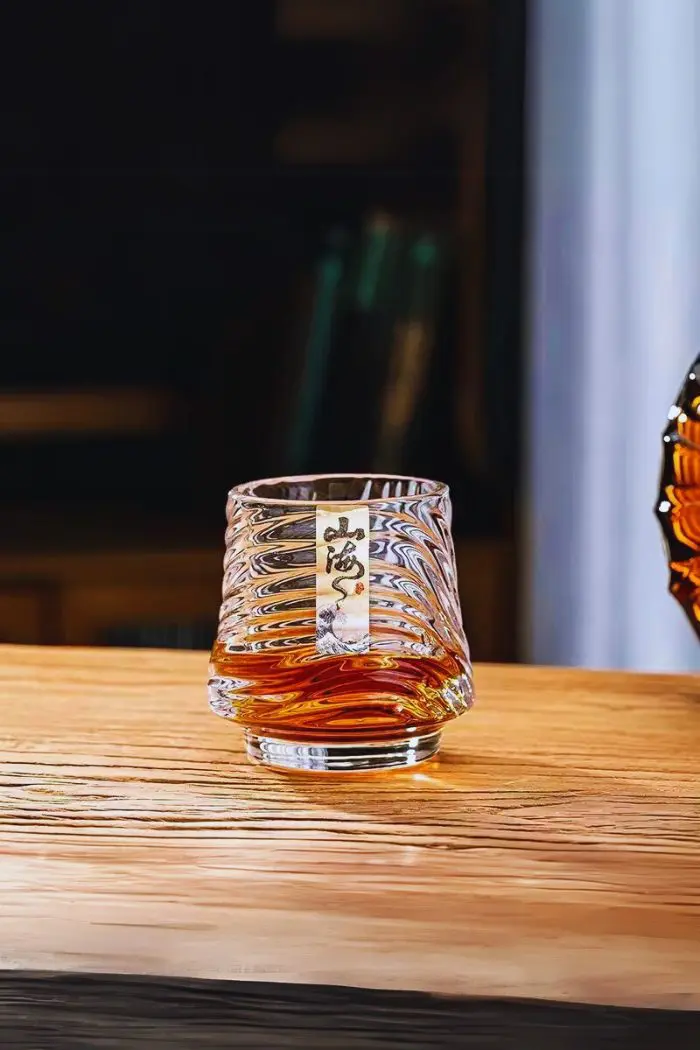 Verre à whisky japonais design mer rempli de whisky ambré, tenu en main