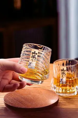 Verre à whisky japonais design mer en cristal transparent, tenu en main, gros plan sur base ondulée