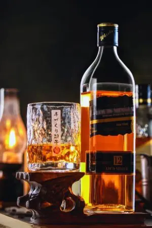 Verre à whisky japonais rond rempli sur socle en bois à côté d'une bouteille de whisky