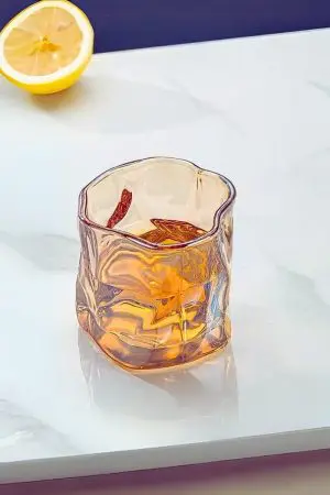 Verre à whisky tumbler ambre à moitié rempli posé sur plateau blanc.