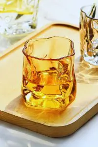 Verre à whisky tumbler ambre vide posé sur plateau en bois clair.