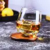 Verre à whisky tumbler incliné sur socle en bois rond, avec glaçon cubique.