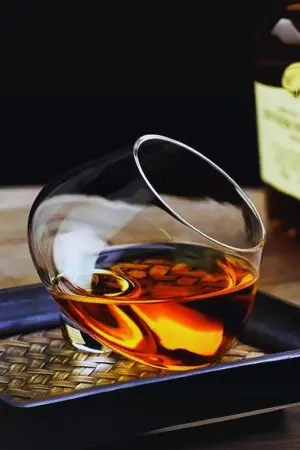 verre à whisky snifter incliné posé sur un plateau texturé avec bouteille floue en arrière-plan