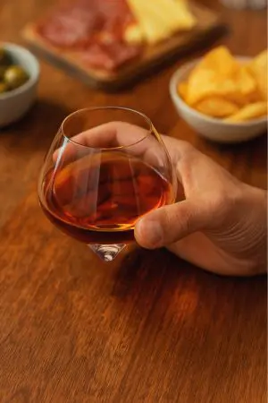 verre à whisky snifter tenu à la main au-dessus d’une table en bois dressée pour l’apéritif