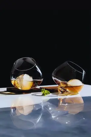 deux verres à whisky snifter inclinés avec glaçons sphériques sur fond noir