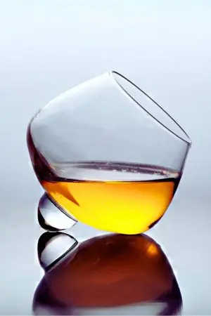 verre à whisky snifter incliné sur fond clair, partiellement rempli de whisky