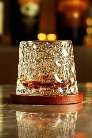 verre à whisky tumbler en cristal transparent posé sur un socle en bois, rempli de whisky, sur table marbrée
