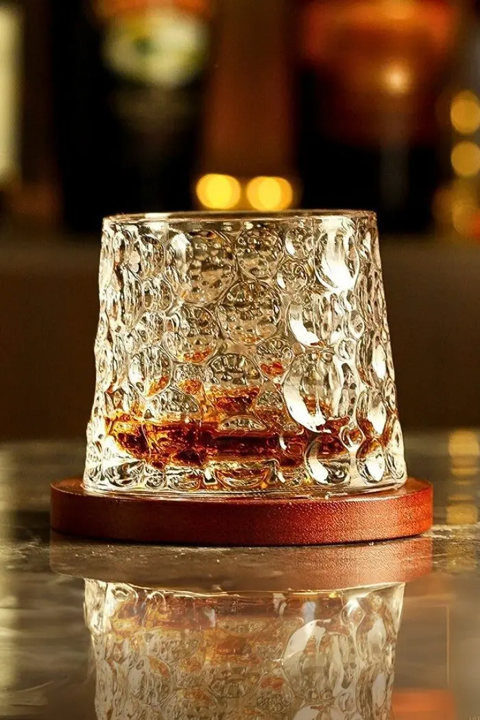 verre à whisky tumbler en cristal transparent posé sur un socle en bois, rempli de whisky, sur table marbrée