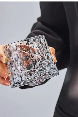 verre à whisky tumbler en cristal texturé tenu en main, incliné