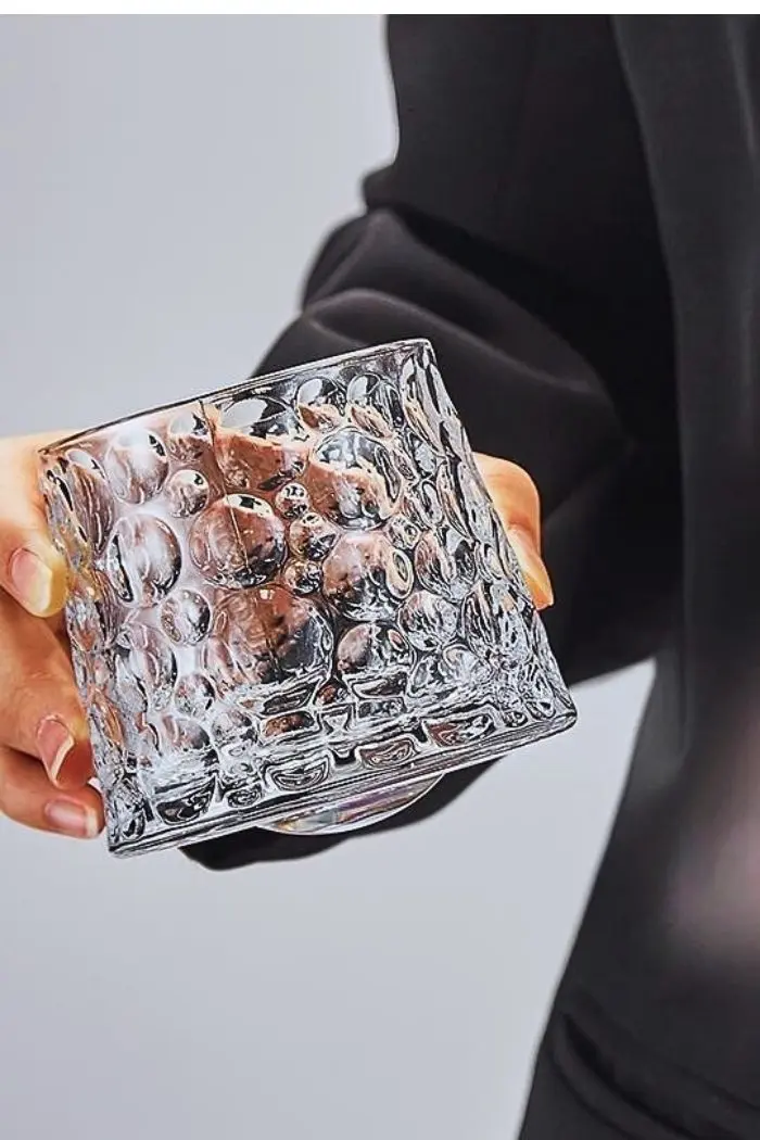 verre à whisky tumbler en cristal texturé tenu en main, incliné