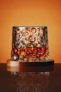 verre à whisky tumbler posé droit sur socle en bois sur fond orange
