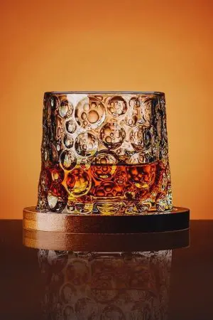 verre à whisky tumbler posé droit sur socle en bois sur fond orange