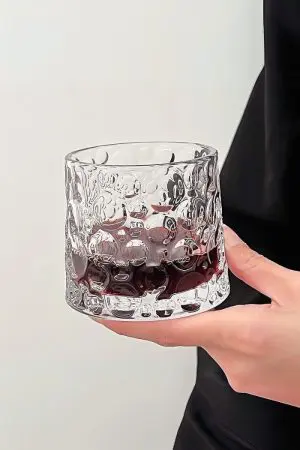verre à whisky tumbler rempli de boisson rouge tenu à deux mains