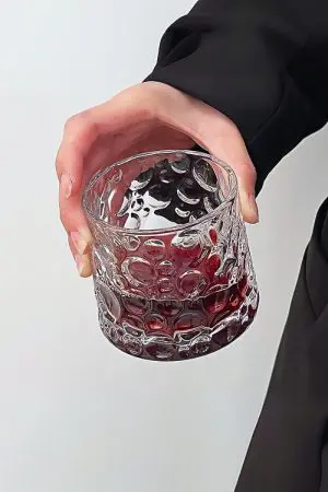 verre à whisky tumbler rempli de boisson rouge incliné dans une main